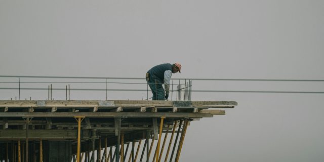 A construction worker bends over rebar on a high framework under a foggy sky in Denizli, Türkiye.